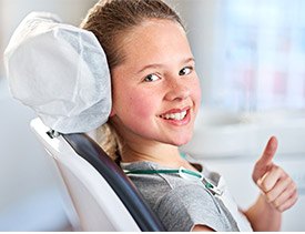 Young girl in dental chair giving thumbs up