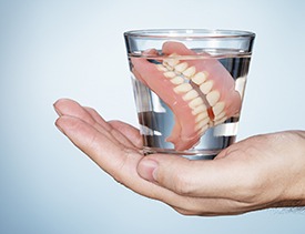 Hand holding full denture in glass of water